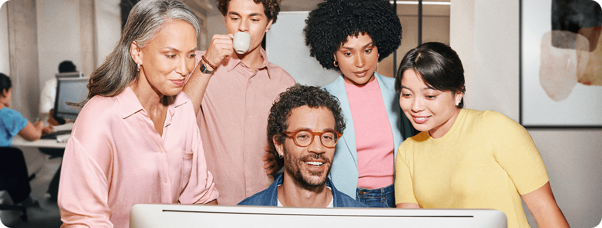 Equipe diversa e multigeracional de cinco colaboradores reunida em volta de um computador.